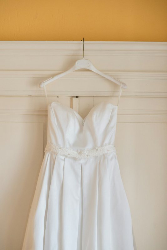 A white strapless dress on a hanger, photographed against a cream door with a yellow wall above.